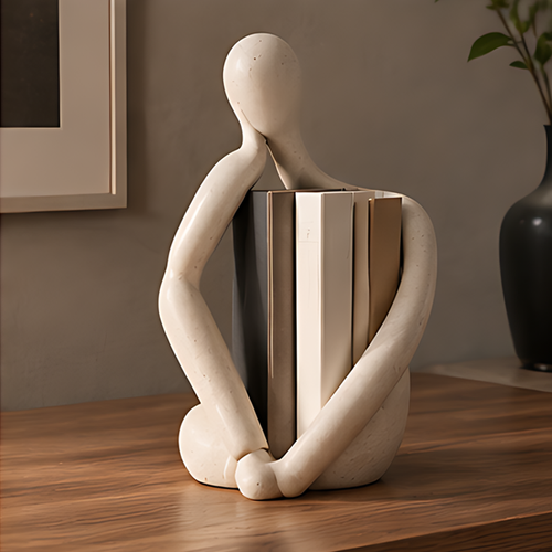 Cream abstract figure bookend sculpture holding books on a wooden shelf with plants and dark vase